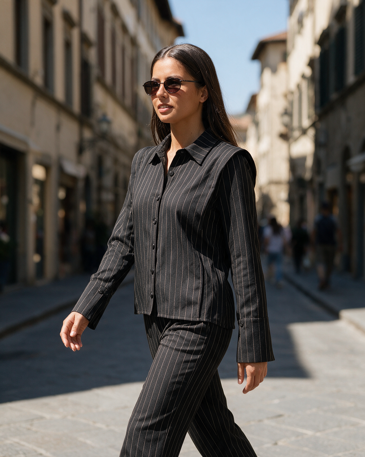 Ženski crni prugasti komplet sa košuljom na preklop i pantalonama ravnog kroja, model hoda ulicom.