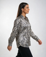 Ženska crno-bela satenska košulja sa zebra printom, klasičnom kragnom i dugim rukavima, nošena uz tamne pantalone.