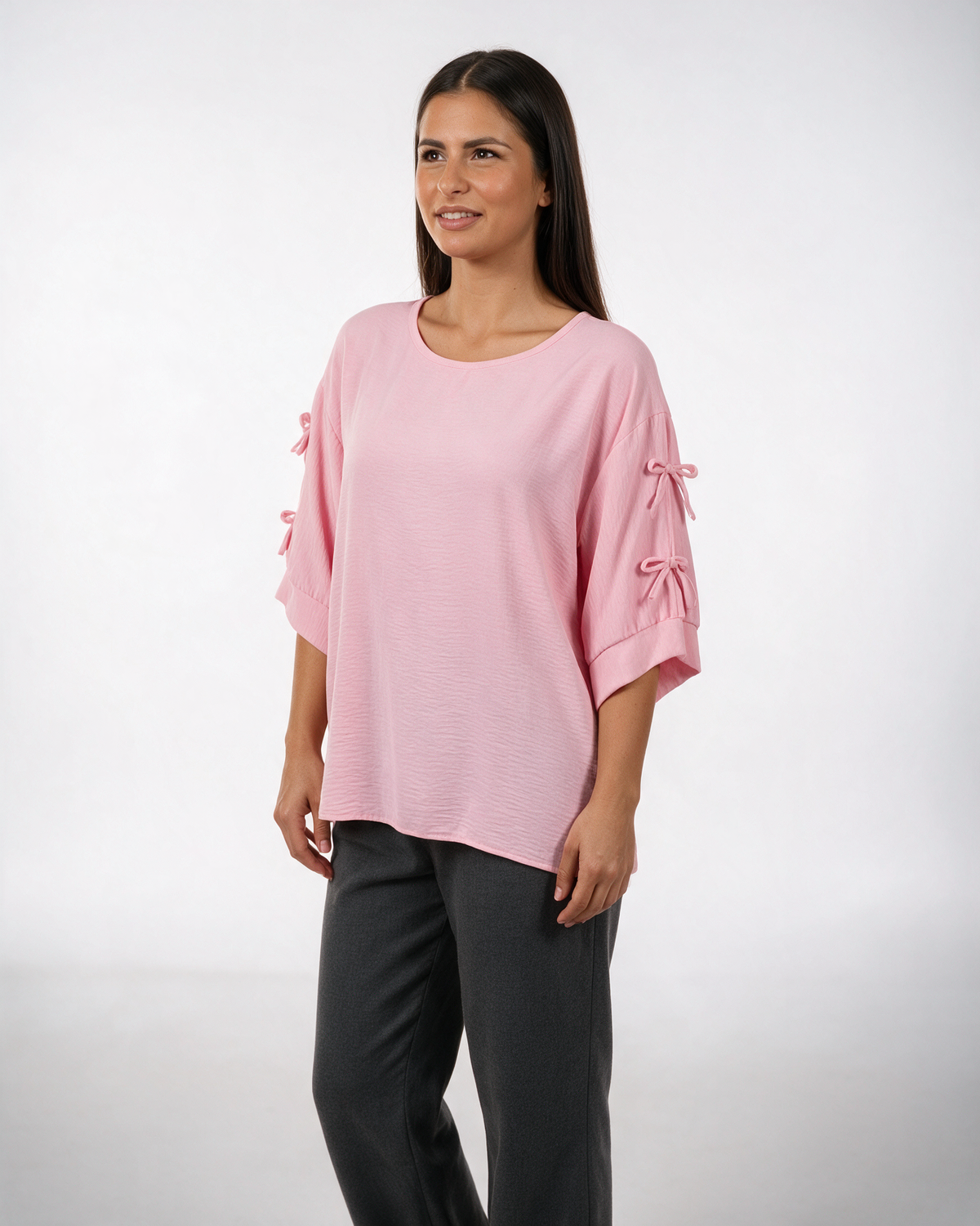 Roze široka bluza sa mašnicama na rukavima, okrugli izrez, krep tkanina, model u belim pantalonama.