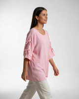 Roze široka bluza sa mašnicama na rukavima, okrugli izrez, krep tkanina, model u belim pantalonama.