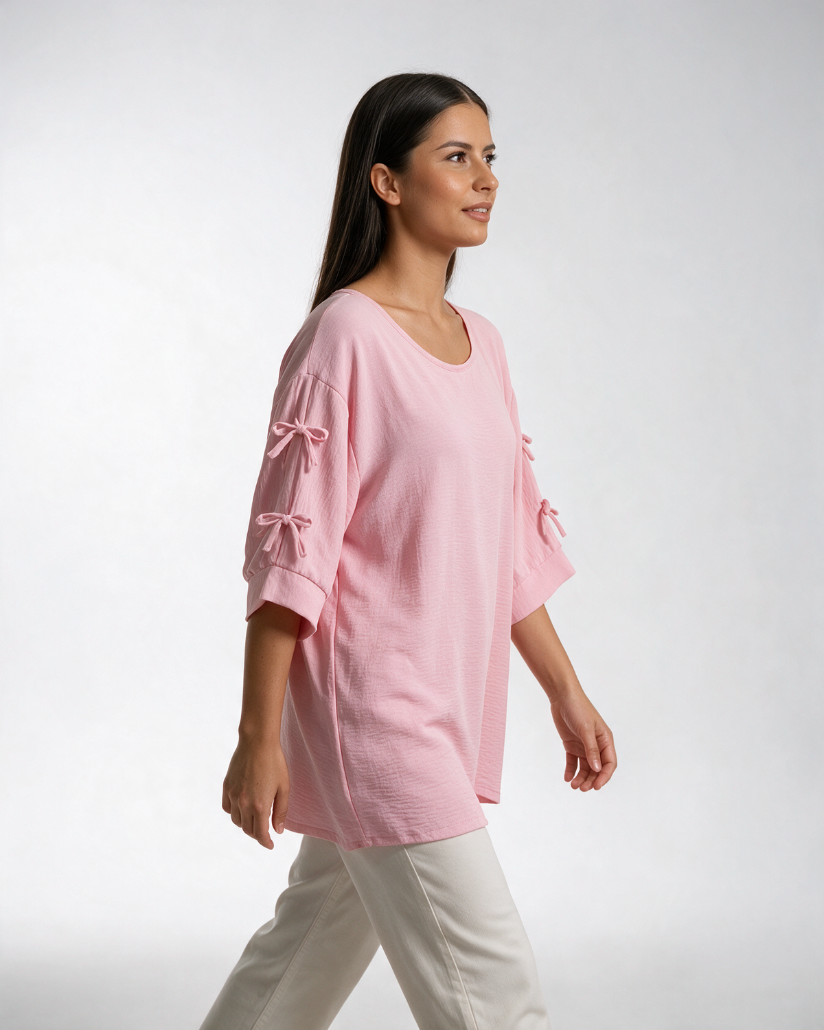 Roze široka bluza sa mašnicama na rukavima, okrugli izrez, krep tkanina, model u belim pantalonama.